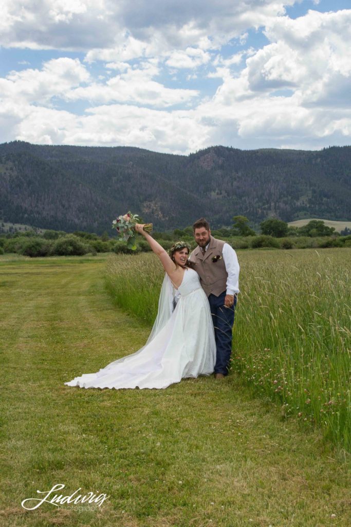 a bride and groom celebrating in a field with mountains in the background