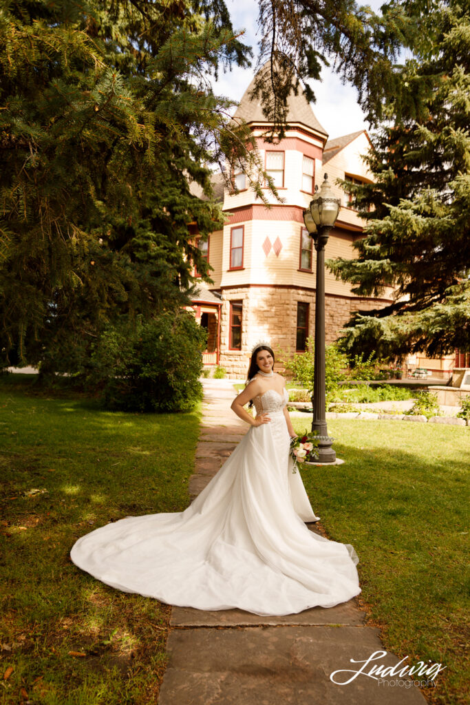 an outdoor portrait of a brunette bride in a wedding gown with the Historic Ivinson Mansion in the background