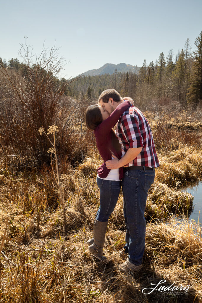 a young couple kissing outdoors by a pond at Pilot Hill in Laramie Wyoming