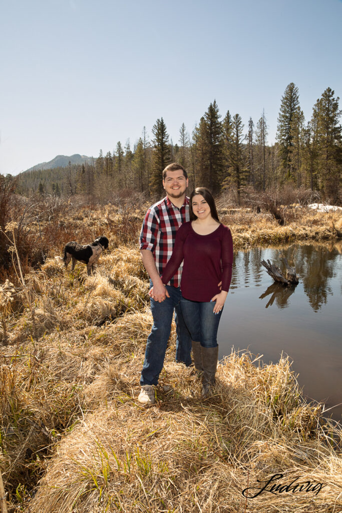 a young couple smiling at the camera outdoors by a pond at Pilot Hill in Laramie Wyoming