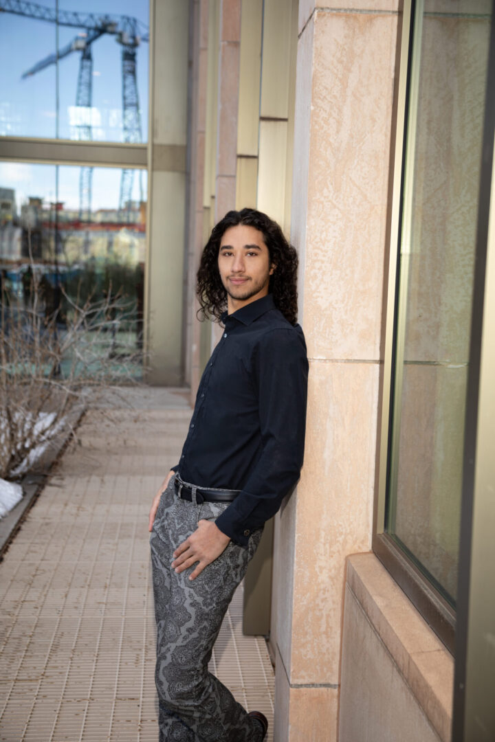 a young man poses for the camera leaning against the college of business university of wyoming laramie. senior and professional photography photographer